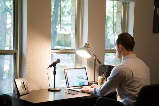 Person sitting at a desk in front of a window working on a laptop